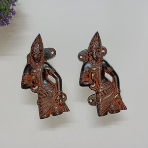 May include: Two ornate black and orange metal door handles with a detailed design of a person holding a flower.