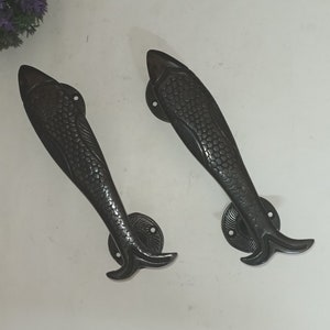 Op de afbeelding: Een paar zwarte metalen deurgrepen in de vorm van een vis. De grepen hebben een gedetailleerd ontwerp met schubben en vinnen.