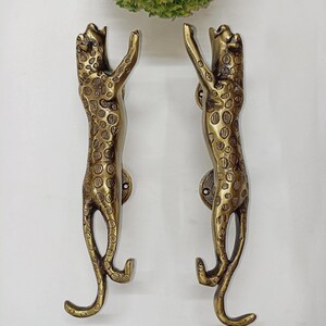 May include: A pair of vertical door handles crafted from brass, each shaped like a leaping leopard with detailed spots and a polished finish. The handles feature mounting plates with visible screw holes, designed for attachment to a door surface.