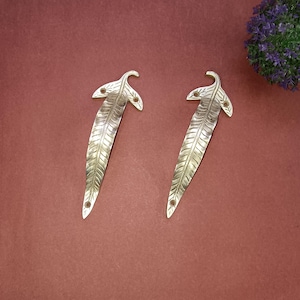 Puede incluir: Dos tiradores de puerta de hoja de plata con un diseño detallado. Los tiradores están sobre un fondo rojo.