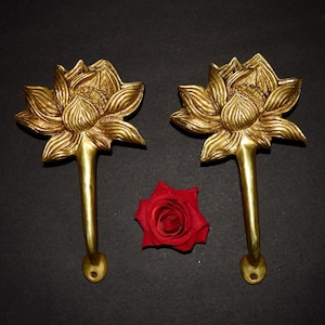 May include: Two gold-colored metal door handles, each featuring a detailed lotus flower design at the top and a straight, smooth handle extending downward with a circular mounting base. A single red rose is positioned between the two handles.