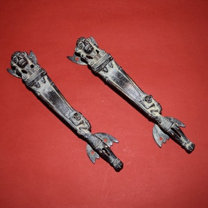 Peut inclure: Une paire de poignées de porte en bronze antique avec des sculptures complexes de figures humaines. Les poignées sont dans un état usé et vieilli, ce qui leur donne un aspect rustique et vintage.