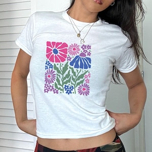 May include: White t-shirt with a colorful floral print design. The flowers are pink, purple, blue, and green.