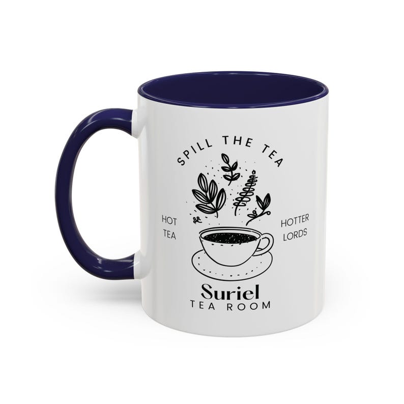Pode incluir: Caneca de cer&acirc;mica branca com borda e al&ccedil;a azul marinho. A caneca apresenta uma ilustra&ccedil;&atilde;o em preto e branco de uma x&iacute;cara de ch&aacute; com vapor saindo dela, cercada por folhas e o texto "Spill the Tea, Hot Tea, Hotter Lords, Suriel Tea Room".
