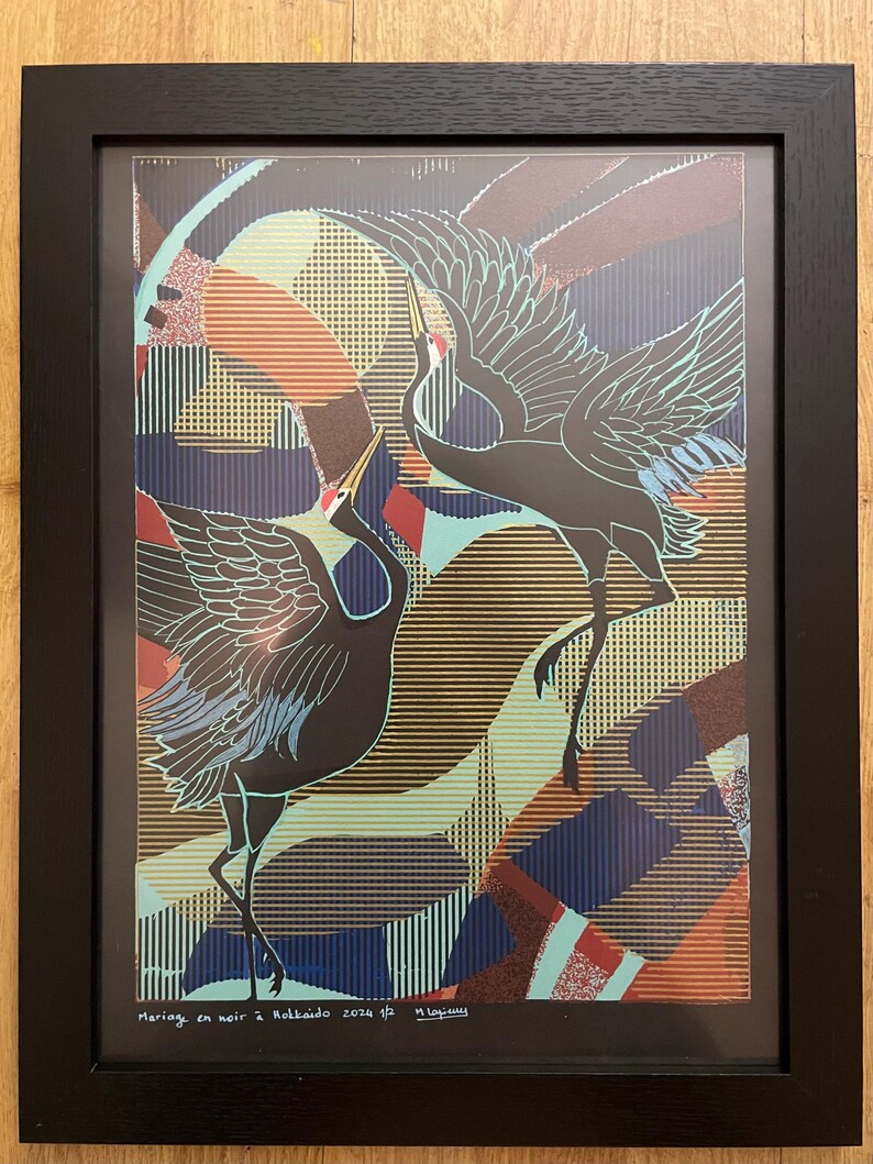 Op de afbeelding: Een ingelijste print van een zwart-witte illustratie van twee kraanvogels in vlucht tegen een kleurrijke geometrische achtergrond. De print is getiteld "mariage en noir" en gesigneerd "Hokkaido 2024 1/2" en "n.ogawa".