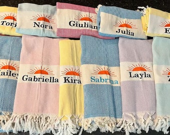 Può includere: Dieci asciugamani da spiaggia personalizzati con un motivo a sole e un nome ricamato su ogni asciugamano. Gli asciugamani sono di vari colori, tra cui blu, rosa, giallo e azzurro.