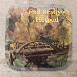 May include: A watercolor painting of a bridge over a river with fall foliage in the background. The text "Fall Bridges Hotpad" is written in yellow at the top of the image.