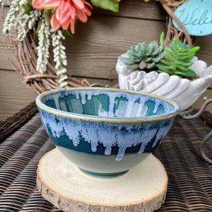 May include: A blue and white ceramic bowl with a drip glaze design. The bowl is sitting on a wooden slice.