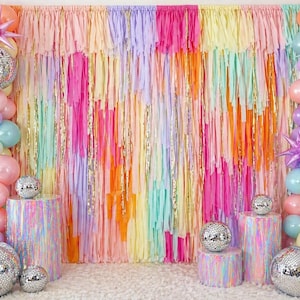 May include: A vibrant party backdrop featuring a rainbow of colors, including pink, yellow, and blue. The backdrop is adorned with streamers and balloons, along with disco balls. The scene is set for a festive celebration.