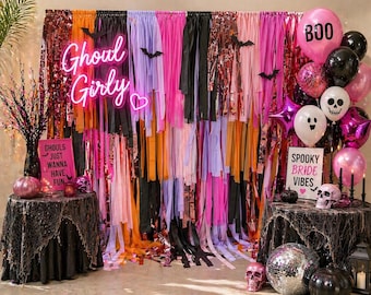 May include: A Halloween-themed party scene with a backdrop of colorful streamers in pink, orange, black, and purple. The words "Ghoul Girly" are in neon. Balloons, skulls, and signs that say "Spooky Bride Vibes" and "Ghouls just wanna have fun" complete the festive decor.