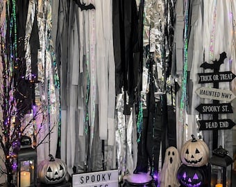 May include: A Halloween-themed display with a backdrop of black, white, and silver streamers and bat decorations. The scene includes pumpkins, skulls, ghosts, a cauldron, and a sign that reads "Spooky Vibes Only".