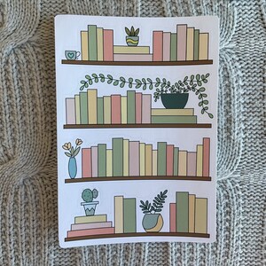 May include: Three sets of stickers featuring bookshelves with different colored books, plants, and a cup of coffee. The bookshelves are brown and the books are in shades of pink, green, yellow, and beige.