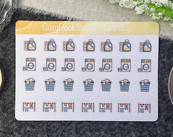 Könnte beinhalten: Ein Blatt mit bunten Aufklebern mit Wäsche-Motiven. Die Aufkleber zeigen Bilder von Waschmittelflaschen, Waschmaschinen, Wäschekörben und Wäscheleinen. Der Text "CozyBookSleeve - Laundry" ist oben auf dem Blatt gedruckt.