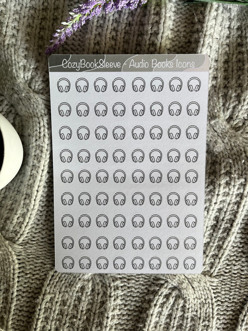 Op de afbeelding: Een vel wit stickerpapier met 64 zwart-witte koptelefoonpictogrammen. Het vel is gelabeld "CozyBookSleeve - Audio Books Icons".