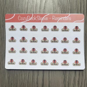 May include: A sheet of stickers with the text "CozyBook Sleeve - Reminders." Each sticker features a red exclamation point inside a white circle, with the word "REMINDER" below. The stickers are on a white background.