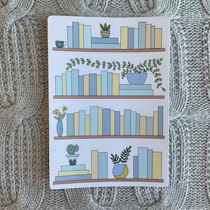May include: A white sticker sheet with four illustrations of bookshelves. Each bookshelf is filled with blue and yellow books and decorated with plants and a small cup of coffee.