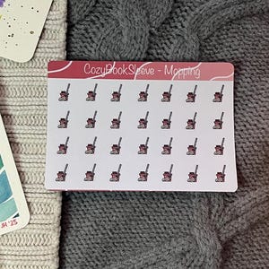 May include: A sheet of stickers with a pink and white border featuring small illustrations of a mop and bucket. The text "CozyBookSleeve - Mopping" is at the top. The stickers are on a white background.