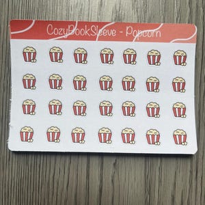 May include: A sheet of stickers featuring small popcorn buckets with red and white stripes, filled with yellow popcorn. The text "CozyBookSleeve - Popcorn" is printed at the top in a handwritten style.