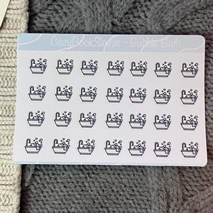 Peut inclure: Une feuille d'autocollants avec un motif répété de petites baignoires remplies de bulles. Les autocollants ont un fond blanc avec un en-tête bleu clair qui indique "CozyBookSleeve - Bubble Bath".
