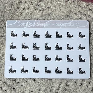May include: A sheet of stickers with black and white hockey skate designs. The text "CozyBookSleeve - Hockey Skates" is printed at the top. The stickers are arranged in rows and columns. The background is a neutral color.