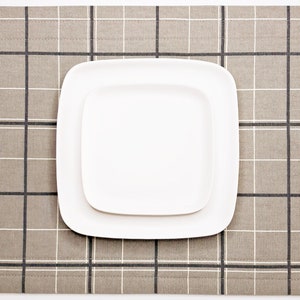 May include: A white square plate sits on a beige placemat with a black and white plaid pattern.