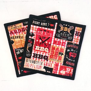 May include: Two square BBQ-themed fabric coasters with black borders. The coasters feature a collage of red, white, and black designs with text like "BBQ Master," "The King of BBQ," and "Roadhouse Grill." The coasters are designed for grilling enthusiasts.