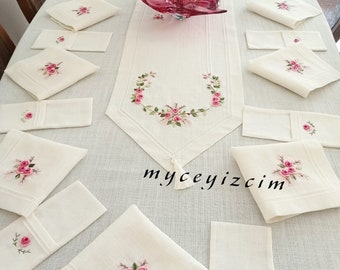 Può includere: Una tovaglia bianca con un runner bianco con rose rosa ricamate. Il runner ha un fiocco all'estremità. Ci sono 15 tovaglioli bianchi con rose rosa ricamate sul tavolo. Il testo "myceyizcim" è visibile sul tavolo.