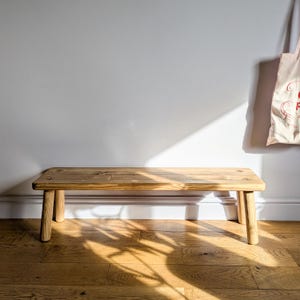 May include: A rustic wooden bench with a natural finish and thick legs. The bench is made of reclaimed wood and has a simple, farmhouse style.