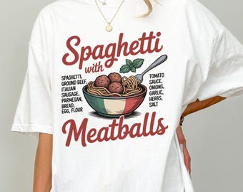 May include: White t-shirt featuring a graphic of spaghetti and meatballs in a bowl. The text on the shirt reads "Spaghetti with Meatballs" with a list of ingredients. The design includes a fork and basil sprig.
