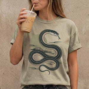 Può includere: Una tazza di ceramica bianca con manico nero e la scritta "But First, Coffee" in grassetto nero. La tazza è posta su uno sfondo sfocato, che suggerisce un'atmosfera accogliente.