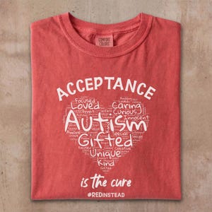 Może przedstawiać: Czerwona koszulka z napisami "ACCEPTANCE" i "Autism" w kształcie serca, wypełniona pozytywnymi słowami, takimi jak "Gifted", "Unique" i "Kind". Widoczny jest również tekst "is the cure" i hashtag "#REDINSTEAD".