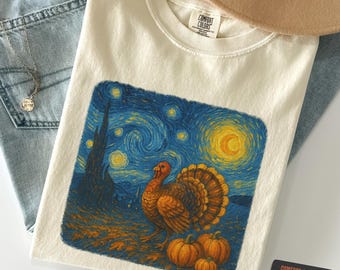 Puede incluir: Camiseta de color marfil con un gráfico colorido de un pavo, calabazas y un cielo estrellado al estilo de Van Gogh. La camiseta está hecha de un material suave y es un Comfort Colors 1717.
