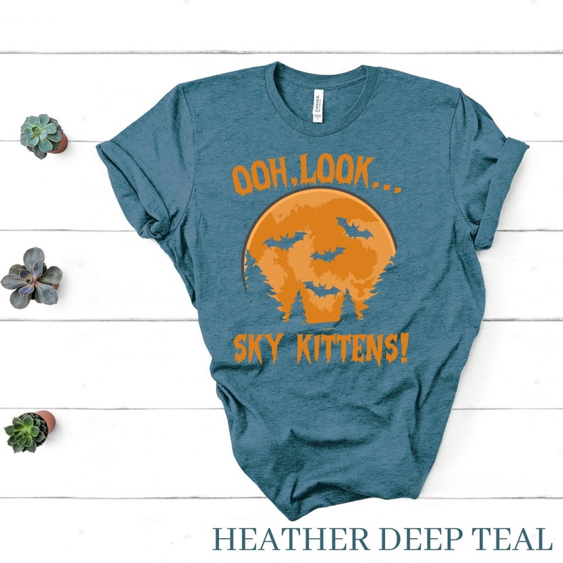 May include: A teal blue t-shirt with a graphic of an orange moon with bats flying around it. The text "Ooh, look... Sky Kittens!" is printed on the shirt.