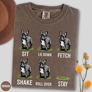 Op de afbeelding: Espresso-kleurig T-shirt met een afbeelding van een Franse bulldog die commando's demonstreert: zit, ga liggen, apporteer, schud, rol om en blijf. Het shirt heeft een Comfort Colors-label en is maat XL-TG-EG.