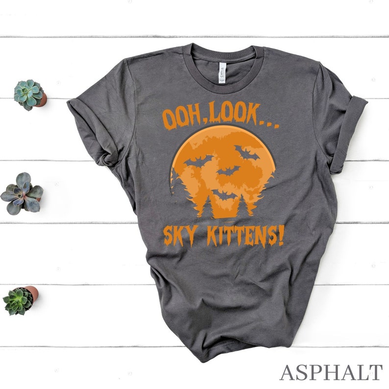 May include: A dark gray t-shirt with an orange moon and bats printed on it. The text "Ooh, look... Sky Kittens!" is printed below the moon.