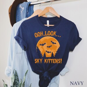 May include: A navy blue t-shirt with a graphic of a full moon and bats. The text "Ooh, look... Sky Kittens!" is printed on the shirt.