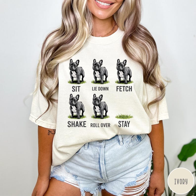 Op de afbeelding: Cr&egrave;mekleurig T-shirt met illustraties van een Franse Bulldog die commando's uitvoert: zit, ga liggen, apporteer, schud, rol om en blijf. De tekst voor elk commando staat onder de bijbehorende afbeelding.