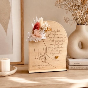 Peut inclure: Une plaque en bois arquée avec un dessin au trait représentant une main d'adulte tenant la main d'un enfant. Le texte indique : Un des plus beaux métiers du monde, c'est prendre un enfant par la main, et l'aider à grandir. MERCI MME MARTEL - MIARO. Ornée d'un petit cœur doré et de fleurs séchées.