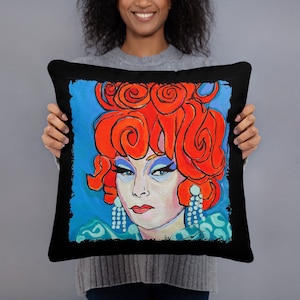 May include: Black throw pillow with a colorful illustration of a person with red hair and blue eyes. The person is wearing a blue and green outfit and large earrings.