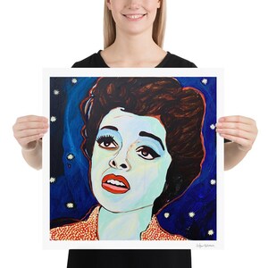May include: A square art print featuring a stylized portrait of a woman with dark hair and red lipstick. The woman's skin is a pale blue, set against a dark blue background with white star accents. The print has a red and orange patterned collar.