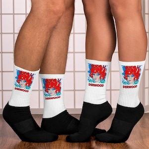 May include: Three pairs of white socks with black cuffs. Each sock features a colorful illustration of a woman with red hair and the word "DERWOOD" printed below the image.