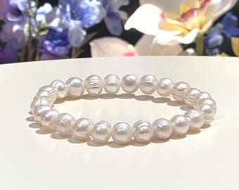 Puede incluir: Una pulsera elástica compuesta por numerosas perlas de agua dulce blancas, brillantes y de forma orgánica. Las perlas están dispuestas en un solo hilo circular continuo, mostrando variaciones naturales en su textura superficial y formas redondeadas.