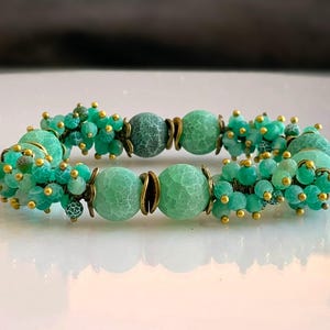 K&ouml;nnte beinhalten: Ein gr&uuml;nes Agat-Armband mit goldenen Akzenten. Das Armband hat auf jeder Seite der gr&ouml;&szlig;eren Agatperlen einen Cluster aus kleineren gr&uuml;nen Perlen.