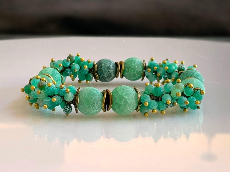 K&ouml;nnte beinhalten: Ein gr&uuml;nes Agat-Armband mit goldenen Akzenten. Das Armband hat auf jeder Seite der gr&ouml;&szlig;eren Agatperlen einen Cluster aus kleineren gr&uuml;nen Perlen.