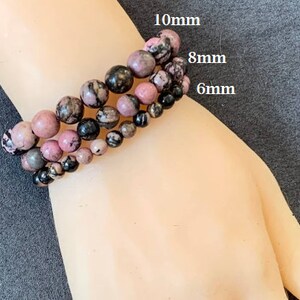 May include: Three bracelets with pink, black, and grey beads. The bracelets feature 10mm, 8mm, and 6mm beads. The bracelets are made of natural stone and are a beautiful accessory.