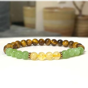 May include: A multi-colored beaded bracelet with green, yellow, and brown beads. The bracelet is made of natural stones.