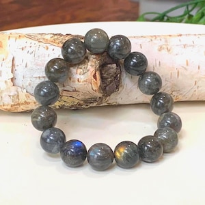 May include: A round beaded bracelet made of gray labradorite stones. The beads are approximately 0.4 inches in diameter. The bracelet is displayed on a piece of birch bark.