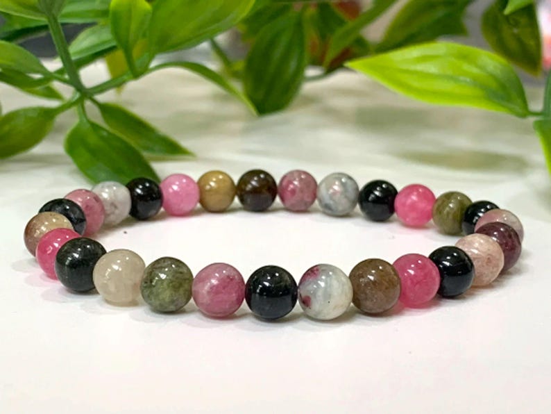 Op de afbeelding: Een armband gemaakt van ronde, veelkleurige edelsteen kralen. De kralen zijn roze, groen, bruin en zwart.
