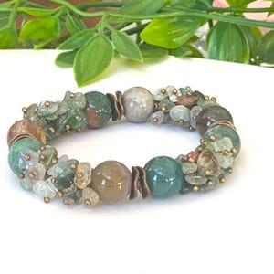 K&ouml;nnte beinhalten: Ein gr&uuml;nes, braunes und wei&szlig;es Edelstein-Armband mit Kupferdraht-Akzenten. Das Armband besteht aus Steinen in verschiedenen Gr&ouml;&szlig;en und Formen.