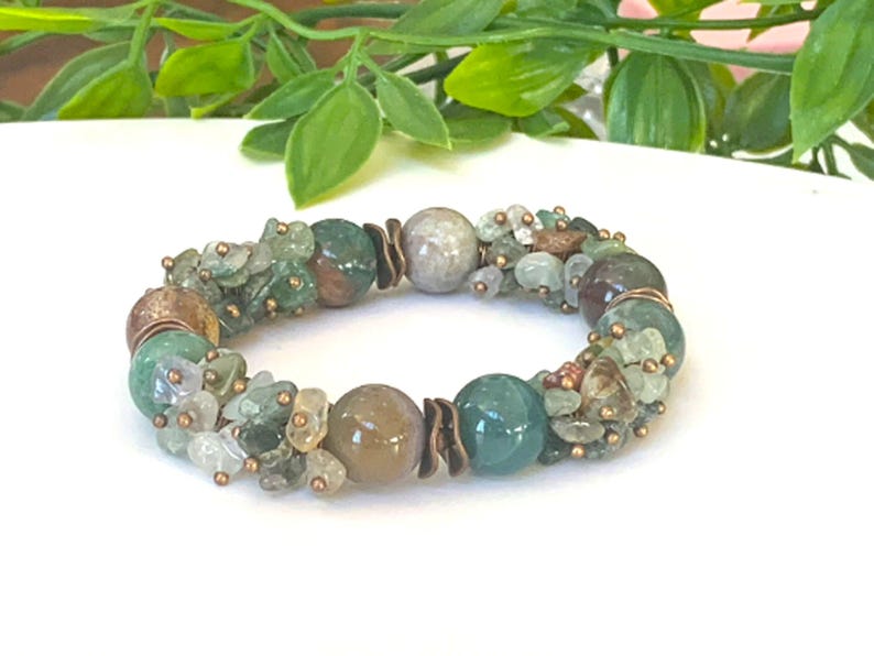 K&ouml;nnte beinhalten: Ein gr&uuml;nes, braunes und wei&szlig;es Edelstein-Armband mit Kupferdraht-Akzenten. Das Armband besteht aus Steinen in verschiedenen Gr&ouml;&szlig;en und Formen.